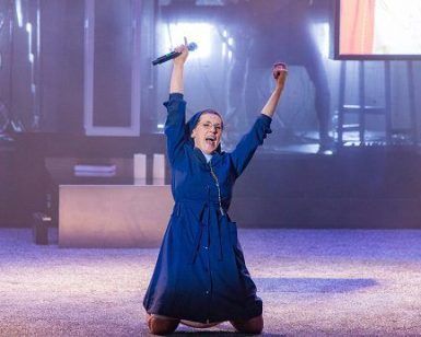 En el Teatro Lara de Madrid, una persona con un vestido azul se arrodilla con los brazos en alto y sostiene un micrófono, lo que recuerda las escenas dinámicas de "La llamada". - ForTwo - Planes para parejas