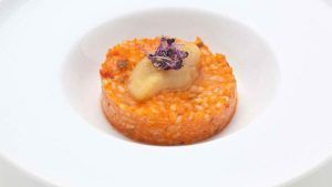 Saborea un risotto gourmet cubierto con erizo de mar y flores moradas comestibles, bellamente presentado en un plato blanco en el Restaurante Las Corchuelas Hospes Palacio de Arenales en Cáceres. - ForTwo - Planes para parejas