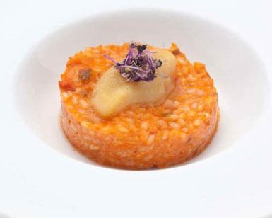 Saborea un risotto gourmet cubierto con erizo de mar y flores moradas comestibles, bellamente presentado en un plato blanco en el Restaurante Las Corchuelas Hospes Palacio de Arenales en Cáceres. - ForTwo - Planes para parejas
