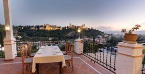Disfrute de una cena romántica en el Restaurante Las Tomasas, donde la terraza ofrece impresionantes vistas del castillo de Granada iluminado en la colina lejana al atardecer. - ForTwo - Planes para parejas