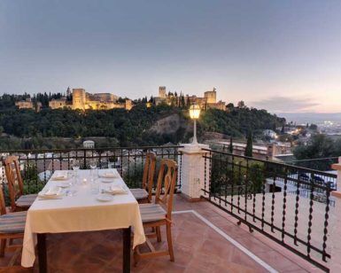 Disfrute de una cena romántica en el Restaurante Las Tomasas, donde la terraza ofrece impresionantes vistas del castillo de Granada iluminado en la colina lejana al atardecer. - ForTwo - Planes para parejas