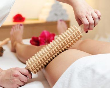 En un tranquilo entorno de spa en Valencia, una persona disfruta de un relajante masaje de piernas utilizando el Tratamiento de Maderoterapia en CosméticaClub Valencia, rodeado de delicados pétalos de rosa. - ForTwo - Planes para parejas