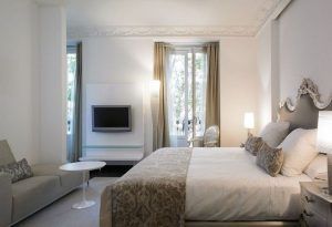 Habitación de lujo en el Hotel Hospes Puerta de Alcalá 5 estrellas Madrid, que ofrece una cama grande, espejo decorativo, sofá, TV y una ventana con cortinas. - ForTwo - Planes para parejas