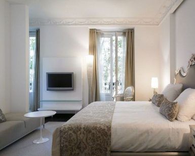 Habitación de lujo en el Hotel Hospes Puerta de Alcalá 5 estrellas Madrid, que ofrece una cama grande, espejo decorativo, sofá, TV y una ventana con cortinas. - ForTwo - Planes para parejas