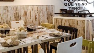 Un comedor rústico incluye una mesa de madera, sillas variadas y vajilla que evoca al Restaurante Mario & Marieta (Cáceres). El arte mural con texto en español añade un encanto vibrante inspirado en Mario & Marieta. - ForTwo - Planes para parejas
