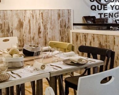 Un comedor rústico incluye una mesa de madera, sillas variadas y vajilla que evoca al Restaurante Mario & Marieta (Cáceres). El arte mural con texto en español añade un encanto vibrante inspirado en Mario & Marieta. - ForTwo - Planes para parejas