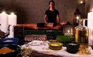 En una serena escena de spa, una persona disfruta de un masaje relajante mientras las velas titilan suavemente. Las ricas fragancias de los aceites Ritual Ancient Argal en Aire de Barcelona impregnan el ambiente, realzando la tranquilidad de este ritual, con cuencos y botellas elegantemente dispuestos en primer plano. - ForTwo - Planes para parejas