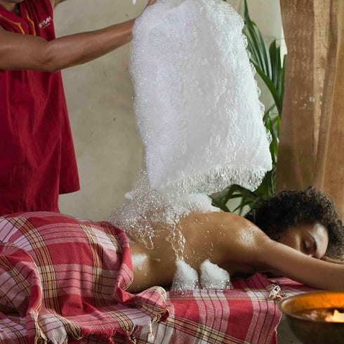 Una persona aprecia el relajante ritual de un masaje con polvos de hierbas sobre una mesa cubierta de cuadros rojos, evocando la atmósfera tranquila del Baño y Ritual Almudaina Para Dos en Hammam Al Ándalus Madrid. - ForTwo - Planes para parejas