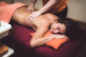 En el centro de bienestar MasVital de Granada, una persona disfruta de un relajante masaje de espalda mientras está tumbada en una camilla cubierta con una toalla naranja durante una sesión en pareja de 45 minutos. - ForTwo - Planes para parejas