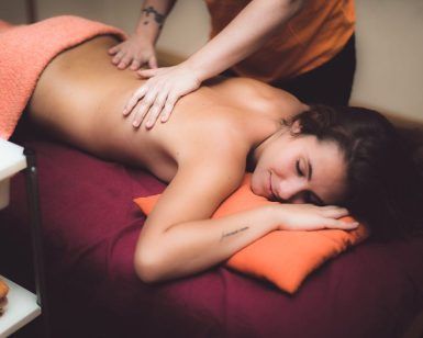 En el centro de bienestar MasVital de Granada, una persona disfruta de un relajante masaje de espalda mientras está tumbada en una camilla cubierta con una toalla naranja durante una sesión en pareja de 45 minutos. - ForTwo - Planes para parejas
