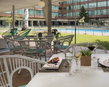 El Day pass “Pool gourmet” del Hotel Meliá Barajas (Madrid) ofrece acceso a un elegante patio exterior con mesas y sillas junto a una resplandeciente piscina, perfecto para disfrutar de comida y bebidas gourmet mientras contempla las vistas a la exuberante zona verde y al señorial edificio. - ForTwo - Planes para parejas