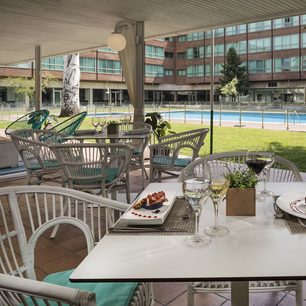 El Day pass “Pool gourmet” del Hotel Meliá Barajas (Madrid) ofrece acceso a un elegante patio exterior con mesas y sillas junto a una resplandeciente piscina, perfecto para disfrutar de comida y bebidas gourmet mientras contempla las vistas a la exuberante zona verde y al señorial edificio. - ForTwo - Planes para parejas
