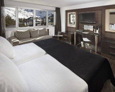 Una moderna habitación del Hotel Meliá Sol y Nieve en Sierra Nevada (Granada) incluye una cama doble, sofá, escritorio y ofrece impresionantes vistas a Sierra Nevada a través de grandes ventanales. - ForTwo - Planes para parejas