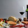 Un delicioso arreglo de Picnic en Barcelona - Menú Montaña con una copa de vino, una botella, pan, queso, carnes, ensalada y frascos se presenta bellamente sobre un fondo gris. - ForTwo - Planes para parejas