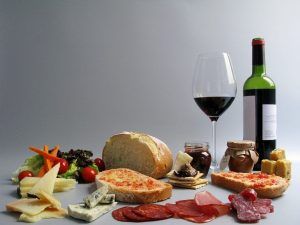 Un delicioso arreglo de Picnic en Barcelona - Menú Montaña con una copa de vino, una botella, pan, queso, carnes, ensalada y frascos se presenta bellamente sobre un fondo gris. - ForTwo - Planes para parejas