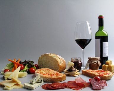 Un delicioso arreglo de Picnic en Barcelona - Menú Montaña con una copa de vino, una botella, pan, queso, carnes, ensalada y frascos se presenta bellamente sobre un fondo gris. - ForTwo - Planes para parejas