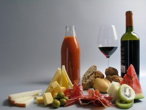 La mesa de picnic está preparada con un delicioso banquete que incluye vino, zumo, quesos, aceitunas, pan, jamón, sandía y kiwi: un Picnic en Barcelona por sorpresa - Menú Mediterráneo perfecto. - ForTwo - Planes para parejas