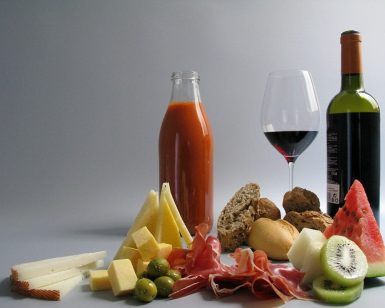 La mesa de picnic está preparada con un delicioso banquete que incluye vino, zumo, quesos, aceitunas, pan, jamón, sandía y kiwi: un Picnic en Barcelona por sorpresa - Menú Mediterráneo perfecto. - ForTwo - Planes para parejas
