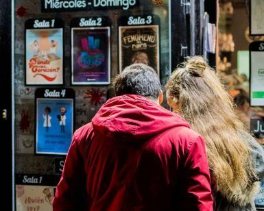 Una pareja se reúne, revisando un cartel de Microteatro que muestra funciones de miércoles a domingo por la noche, contemplando ansiosamente Entradas al Microteatro (Madrid) para sus planes nocturnos. - ForTwo - Planes para parejas