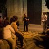 Un guía de "Tour guiado por los misterios de Córdoba" acompaña a un grupo sentado en un camino de piedra bajo el cielo nocturno, cerca de un gran muro. - ForTwo - Planes para parejas