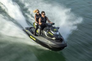 Dos personas en una "Surca las olas de Barcelona en moto acuática" navegan rápidamente sobre el agua, creando un chapoteo tras de sí. - ForTwo - Planes para parejas