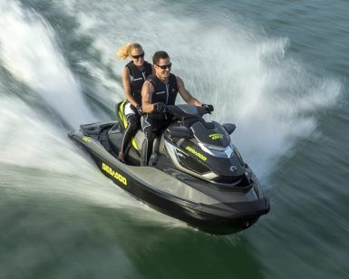 Dos personas en una "Surca las olas de Barcelona en moto acuática" navegan rápidamente sobre el agua, creando un chapoteo tras de sí. - ForTwo - Planes para parejas