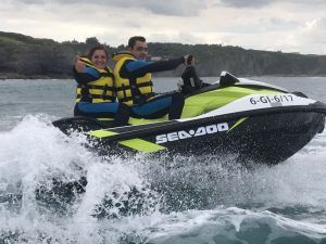 Dos personas, ataviadas con chalecos salvavidas amarillos, disfrutan de un emocionante paseo sobre las olas del océano cerca de los acantilados rocosos de Gijón con Excursión motos de agua (Gijón). - ForTwo - Planes para parejas
