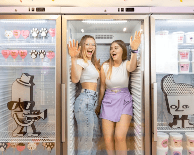 Dos mujeres ríen dentro de una gran nevera adornada con divertidas calcomanías de dibujos animados y envases de helado en el peculiar Museo Sweet Space de Madrid. ¡Compra tus "Entradas al Museo Sweet Space de Madrid" para vivir una experiencia encantadora!. - ForTwo - Planes para parejas