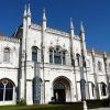 Un edificio histórico de piedra blanca con arcos y agujas ornamentados bajo un cielo azul despejado. Los carteles a la entrada guían a los visitantes para explorar estos monumentos, accesibles con la Lisboa Card: tarjeta con descuentos para acceder a los monumentos. - ForTwo - Planes para parejas