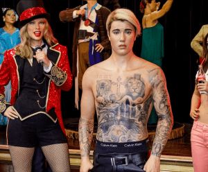 Las figuras de cera de una mujer con chaqueta roja y micrófono, y de un hombre tatuado, sin camisa y con pantalones negros, se alzan imponentes en el Museo de Cera de Madrid. Estas creaciones esculpidas de gran realismo forman parte de las impresionantes exposiciones que puedes explorar con tus Entradas al Museo de Cera de Madrid. - ForTwo - Planes para parejas