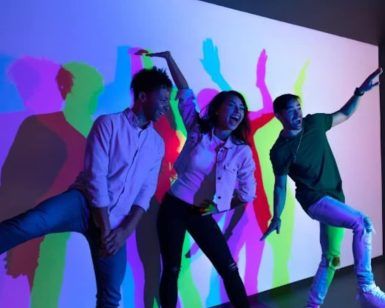Tres personas en poses divertidas frente a un fondo colorido y lleno de sombras en el Museo de las Ilusiones de Sevilla. - ForTwo - Planes para parejas