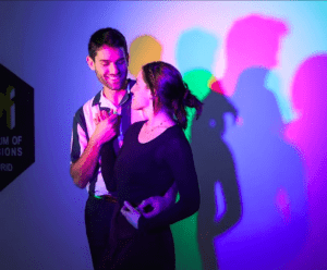 En el Museo de las Ilusiones de Madrid, una pareja posa juguetonamente, creando sombras de colores bajo luces rosas, azules y verdes. ¡Reserva ya tus entradas al Museo de las Ilusiones de Madrid para disfrutar de esta vibrante experiencia!. - ForTwo - Planes para parejas