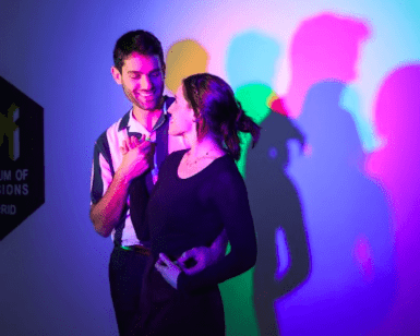 En el Museo de las Ilusiones de Madrid, una pareja posa juguetonamente, creando sombras de colores bajo luces rosas, azules y verdes. ¡Reserva ya tus entradas al Museo de las Ilusiones de Madrid para disfrutar de esta vibrante experiencia!. - ForTwo - Planes para parejas