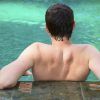Una persona con el pelo corto se apoya en el borde de una piscina serena en Circuito spa y smoothie en NQ TAKE AWAY & SPA WELLNESS NATURQUINOA en Madrid, contemplando el agua tranquila y capturando un momento de puro bienestar. - ForTwo - Planes para parejas