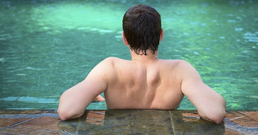 Una persona con el pelo corto se apoya en el borde de una piscina serena en Circuito spa y smoothie en NQ TAKE AWAY & SPA WELLNESS NATURQUINOA en Madrid, contemplando el agua tranquila y capturando un momento de puro bienestar. - ForTwo - Planes para parejas