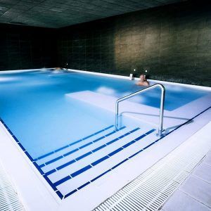 En Spa O2 Granada, la Oferta: Circuito ofrece una experiencia de relax en una piscina cubierta de agua cristalina y escaleras, rodeada de paredes de azulejos oscuros. - ForTwo - Planes para parejas
