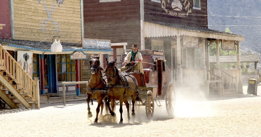 Una diligencia tirada por dos caballos recorre un polvoriento pueblo del Oeste, que recuerda a Oasys, el parque temático del desierto de Tabernas (Almería). Ofrece una vívida mirada al pasado sin necesidad de entradas. - ForTwo - Planes para parejas
