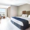 Experimente un lujo inigualable en una moderna habitación de hotel con una cama grande, escritorio de madera, silla, lámpara y amplios ventanales que dan a un balcón con serenas vistas a Cala Talamanca. Disfrute de esta exquisita escapada a Ibiza con la "Escapada de lujo en Cala Talamanca con desayuno". - ForTwo - Planes para parejas