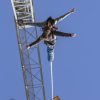 Una pareja atrevida se lanza al puenting desde una grúa contra el cielo azul claro de Barcelona, disfrutando del "Puenting en Barcelona en pareja". - ForTwo - Planes para parejas