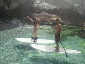 Dos personas y un perro disfrutan del paddle surf en la cristalina y rocosa cala de Cantarriján utilizando las tablas de stand-up de la "Ruta de Paddle Surf en Cantarriján". - ForTwo - Planes para parejas