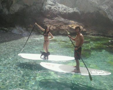 Dos personas y un perro disfrutan del paddle surf en la cristalina y rocosa cala de Cantarriján utilizando las tablas de stand-up de la "Ruta de Paddle Surf en Cantarriján". - ForTwo - Planes para parejas