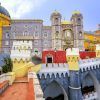 Ubicada en las vibrantes afueras de Lisboa, la "Excursión por los alrededores más turísticos de Lisboa" ofrece una visita a un colorido palacio con torres amarillas, rojas y grises adornadas con arcos y detalles intrincados bajo un cielo azul sereno, ideal para una excursión. - ForTwo - Planes para parejas