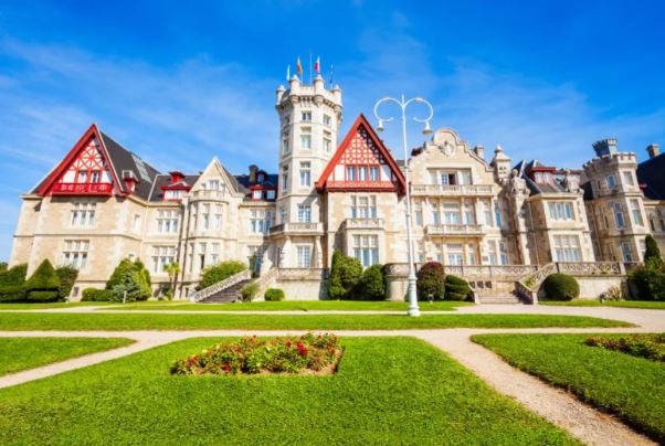 Explora la Visita al Palacio de la Magdalena en Santander, donde la arquitectura elaborada se combina con exuberantes jardines verdes bajo un cielo azul claro. - ForTwo - Planes para parejas