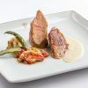 Un plato gourmet con dos suculentas carnes en salsa cremosa y verduras mixtas sobre un plato cuadrado blanco evoca las refinadas experiencias culinarias del Restaurante Torreorgaz Parador de Cáceres. - ForTwo - Planes para parejas