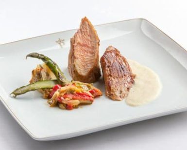 Un plato gourmet con dos suculentas carnes en salsa cremosa y verduras mixtas sobre un plato cuadrado blanco evoca las refinadas experiencias culinarias del Restaurante Torreorgaz Parador de Cáceres. - ForTwo - Planes para parejas
