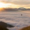 Un parapente disfruta de una impresionante experiencia de vuelo en parapente a diferentes alturas en Tenerife, elevándose por encima de las nubes al atardecer, con majestuosas montañas y el sol creando un impresionante telón de fondo. - ForTwo - Planes para parejas