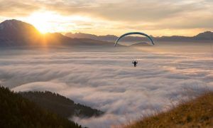 Un parapente disfruta de una impresionante experiencia de vuelo en parapente a diferentes alturas en Tenerife, elevándose por encima de las nubes al atardecer, con majestuosas montañas y el sol creando un impresionante telón de fondo. - ForTwo - Planes para parejas