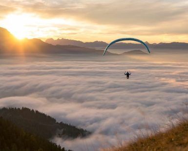 Un parapente disfruta de una impresionante experiencia de vuelo en parapente a diferentes alturas en Tenerife, elevándose por encima de las nubes al atardecer, con majestuosas montañas y el sol creando un impresionante telón de fondo. - ForTwo - Planes para parejas