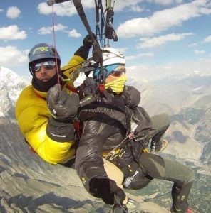 Dos personas disfrutan de un "Vuelo en parapente en Granada" sobre un impresionante paisaje montañoso, equipados con ropa de abrigo y cascos. - ForTwo - Planes para parejas