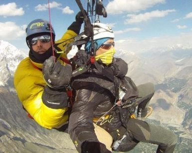 Dos personas disfrutan de un "Vuelo en parapente en Granada" sobre un impresionante paisaje montañoso, equipados con ropa de abrigo y cascos. - ForTwo - Planes para parejas